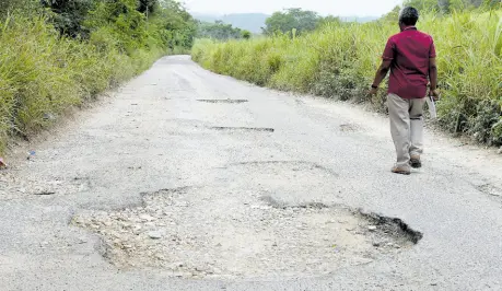  ?? ?? A man walks along a pothole-riddled section of the main road from Duncans to Clark’s Town in Trelawny.