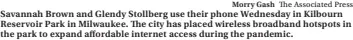  ?? Morry Gash The Associated Press ?? Savannah Brown and Glendy Stollberg use their phone Wednesday in Kilbourn Reservoir Park in Milwaukee. The city has placed wireless broadband hotspots in the park to expand affordable internet access during the pandemic.