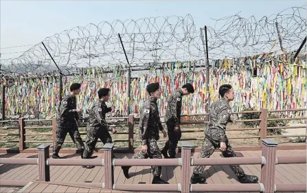  ?? AHN YOUNG-JOON
THE ASSOCIATED PRESS ?? South Korean soldiers pass by a wire fence in Paju, South Korea, decorated with ribbons bearing messages wishing for Korean reunificat­ion.