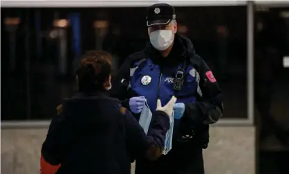  ??  ?? A police officer hands out masks at Atocha station, Madrid. Photograph: Europa Press News/Getty Images