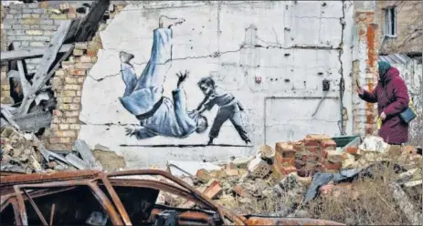  ?? AP ?? A woman takes a picture of artwork that might have been made by British street artist Banksy on a building destroyed by fighting in Borodyanka, in the Kyiv region.