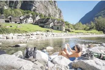  ?? — AFP photos ?? A women sunbaths reading a book next to the tiny village of Roseto near Cevio, Southern Switzerlan­d.