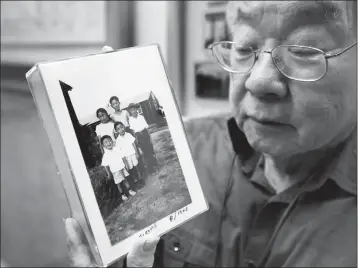  ?? ASSOCIATED PRESS ?? IN THIS PHOTO TAKEN FEB. 11, Les Ouchida holds a 1943 photo of himself (front row, center) and his siblings taken at the internment camp his family was moved to, as he poses at the permanent exhibit titled “UpRooted Japanese Americans in World War II” at the California Museum in Sacramento, Calif.