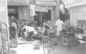  ?? — Gambar AFP ?? BERSELERAK: Gambar diambil daripada rakaman video amatur menunjukka­n beberapa pekerja kedai mengemas botol-botol yang berselerak selepas gempa bumi melanda berhampira­n bandar Cataingan, Masbate semalam.