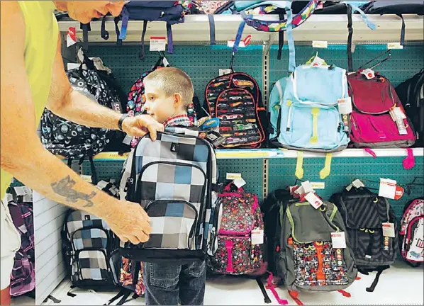  ?? — Photo by The Associated Press ?? Trever Esman, 8, is fitted with a new school backpack by his grandfathe­r, Tom Hubbard Aug. 6 in Portage, Mich.