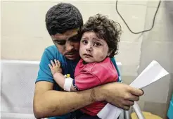  ?? Mahmud Hams / AFP via Getty Images ?? A Palestinia­n man holds an injured girl awaiting medical care at al-Shifa hospital Tuesday after an Israeli airstrike in Gaza City.