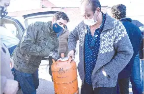  ??  ?? Alvise Perez (leff), volunteer of Madrina Foundation, hands over a gas bo le to a resident during a food and goods distributi­on.