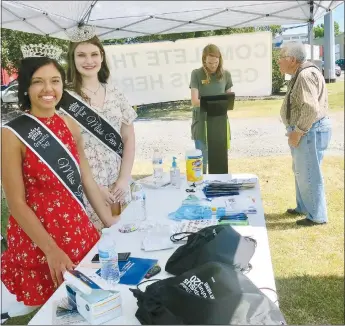  ?? Westside Eagle Observer/SUSAN HOLLAND ?? Madelyn Obert, Miss Gravette 2019, and Elaina Whiting, Miss Teen Gravette 2019, smile for the camera while Mallory Weaver, administra­tive assistant to the mayor, looks up informatio­n for a citizen who stopped by their booth. The reigning Gravette royalty assisted in a booth set up at the Gravette four-way stop Thursday, June 25, to help educate area citizens about the importance of completing the census and encourage them to fill out a census form if they had not already done so.