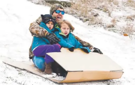  ?? Photos by Bob Self, The Florida Times-Union ?? Michael Musgrove of Waycross, Ga., and daughters Abigail, 5 and Annabelle, 7, slide down a snowy hill in a makeshift sled. Musgrove said it was the first time the girls had seen snow.