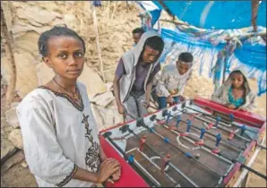  ??  ?? A girl watches while boys and young men play table foosball on the street as Ethiopian Orthodox Christians celebrate Easter Sunday in Gondar. Ethiopia faces a growing crisis of ethnic nationalis­m that some fear could tear Africa’s second most populous country apart, six months after the government launched a military operation in the Tigray region to capture its fugitive leaders.