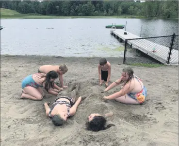  ?? TANIA BARRICKLO — DAILY FREEMAN ?? Madison Cuzzta, 15, lying at left, and her stepsister, Lexi Potter, also 15, get buried in the sand by friends on Tuesday, July 7, at the village beach in Saugerties, N.Y., along the Esopus Creek. Applying the sand are, from left, Taylor Stahli, 11, Keighan Vaughan, 12, Spencer Hansel, 11, and Atalyah Vaughan, 11. All of the youngsters live in Saugerties.