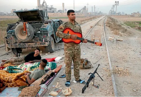  ??  ?? An Iraqi special forces policeman strums a guitar while he and his comrades grab some rest during their advance near Karamah, south of Mosul.
