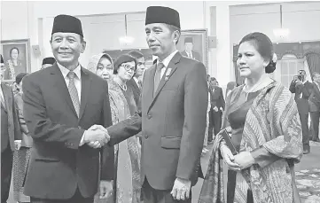  ?? — AFP photo ?? Widodo (centre right) s hakes hands with Wiranto during an inaugurati­on ceremony at the presidenti­al palace in Jakarta.