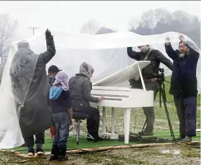  ??  ?? Chinese contempora­ry artist Ai Weiwei ( right) protects himself and others from the rain, as nour Al Khizam ( centre) from the city Deirez Zor, syria, plays the piano during a performanc­e at a refugee camp, at the border of Greece and Macedonia.