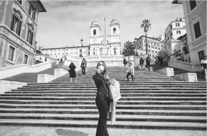  ?? Andrew Medichini / Associated Press ?? A woman wearing a dust mask poses for photos at the bottom of the Spanish Steps in Rome. The focal point of the coronaviru­s emergency in Europe, Italy also is the region’s weakest economy and is taking a hit as foreigners stop visiting.