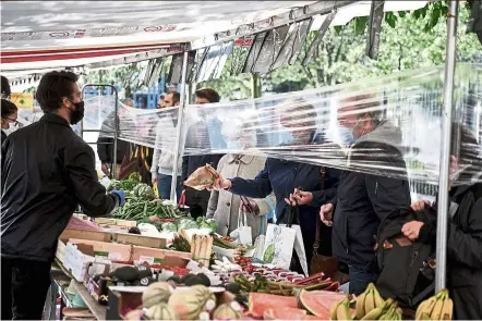  ?? — AFP ?? a seller attending to customers standing behind a single-use plastic ‘barrier’ at a Paris market recently. Plastic and plastic products have become crucial accessorie­s to keep Covid-19 at bay.