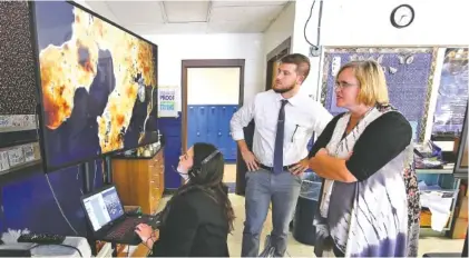  ?? STAFF PHOTO BY ERIN O. SMITH ?? Amal Abazid, left, a Red Bank High senior; Cameron Huss, center, a Project Inspire resident; and Dani Morris, a biology teacher at Red Bank High School, look at organisms on a television screen streamed Thursday. Students in an advanced placement biology class at Red Bank are able to use the 4K streaming capability provided by EPB’s high-speed fiber optic network to remotely connect to the DX63 Darkfield microscope at the STEM school at Chattanoog­a State Community College.