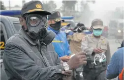  ?? AMAN ROCHMAN/ AFP/ GETTY IMAGES ?? Indonesian police distribute face masks to residents on the streets of Malang, East Java province Friday as volcanic ash covered the city.