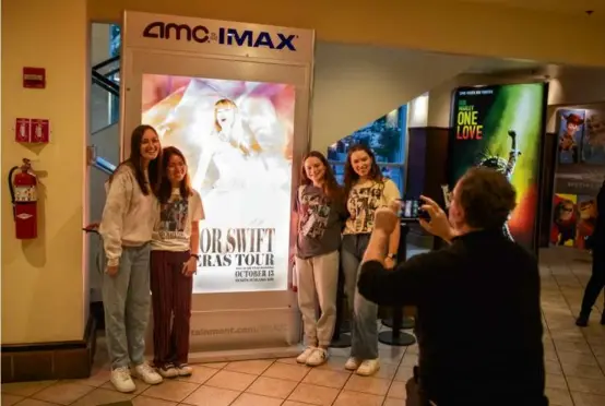  ?? PHOTOS BY NATHAN KLIMA FOR THE BOSTON GLOBE ?? A group posed for a picture in front of a sign for the “Taylor Swift: The Eras Tour” film at AMC Boston Common on Thursday.