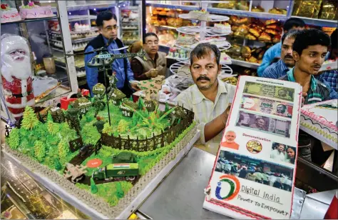  ?? AFP ?? Shoppers gather to purchase cakes—one prepared in the theme of demonetisa­tion (R) and another on the recent “surgical strike” military action in the border region with Pakistan—at a bakery on Christmas Eve in Siliguri on Saturday. Earlier this week, UK...
