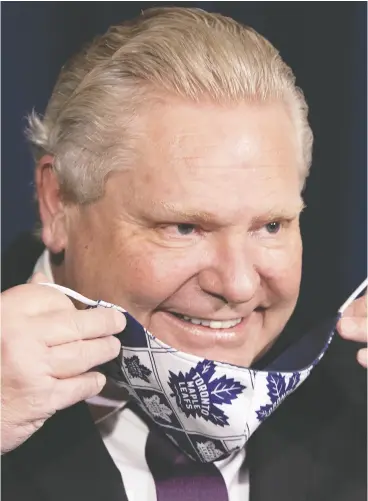  ?? FRANK GUNN / THE CANADIAN PRESS ?? Ontario Premier Doug Ford puts on his Toronto Maple Leafs mask during his daily briefing in Toronto on Monday, where he announced an easing of COVID restrictio­ns.