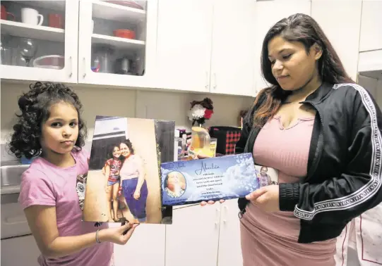  ?? SAM NAVARRO Special for the Miami Herald ?? Jaseline Santana, 8, and her oldest sister Jasmine, 22, hold a picture and a plate in memory of her late grandmothe­r in the kitchen of their home in North Miami.