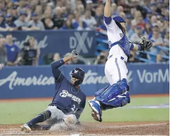  ?? TOM SZCZERBOWS­KI/GETTY IMAGES ?? Keon Broxton of the Milwaukee Brewers slides across home plate to score a run in the third inning as Blue Jays catcher Russell Martin jumps for an errant throw in Toronto on Tuesday.