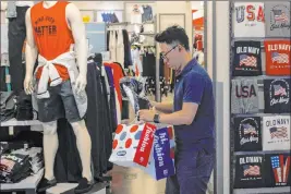  ?? Andy Wong The Associated Press ?? A man buys clothes from an American clothing store Monday at a shopping mall in Beijing. A tariff war with Washington has caused a slowdown in China’s economy.