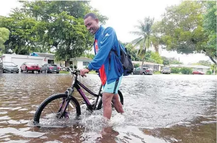  ?? JOECAVARET­TA/SOUTHFLORI­DASUNSENTI­NEL ?? Amanwalks his bike through a flooded streetMond­ay in the Melrose Place neighborho­od of Fort Lauderdale.