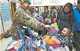  ?? MARK THIESSEN/AP ?? Alaska National Guard Staff Sgt. Joseph Sallaffie hands a gift bag to Corban Jimmy while Marlene Black looks on during Santa’s visit to Napakiak, Alaska.