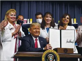  ?? ALEX BRANDON — THE ASSOCIATED PRESS ?? President Donald Trump, flanked by health care workers, holds up a signed executive order on lowering drug prices during a ceremony at the White House on Friday.