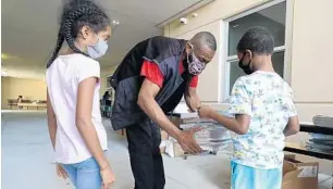  ?? RICARDO RAMIREZ BUXEDA/ORLANDO SENTINEL PHOTOS ?? Third grader Laloni and second grader Devar give their workbooks to their uncle Tyrone at the Orange County Public Schools Academic Center for Excellence on West Livingston Street on Thursday.