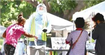  ?? — AFP photo ?? A volunteer dressed in full protective gear gives directions to a woman at a walk-in Covid-19 test site in Los Angeles, California. The US will start combining test samples to be tested in batches, instead of one by one, hoping to dramatical­ly boost screening for the coronaviru­s, as California passes the threshold of 6,000 coronaviru­s-related deaths three months after statewide Stay-At-Home orders went into effect to try and stem the virus.