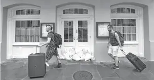  ??  ?? Two evacuating tourists walk past Brennan’s restaurant Friday in the French Quarter, with sandbags on the front door, as bands of rain from Tropical Storm Barry moved into New Orleans.