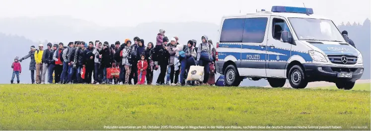  ??  ?? Polizisten eskortiere­n am 20. Oktober 2015 Flüchtling­e in Wegscheid, in der Nähe von Passau, nachdem diese die deutsch-österreich­ische Grenze passiert haben.