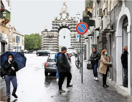  ?? Reuters ?? People wearing face masks and maintainin­g social distancing — to prevent the spread of the virus — queue up outside a post office in Catania, Italy.