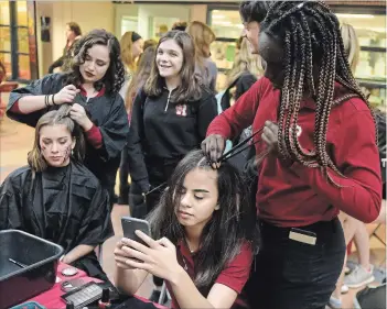  ?? PHOTOS BY DAVID BEBEE , WATERLOO REGION RECORD ?? Left photo: Rachel Vezsenyi, left, has her hair done by Natasha Kircos, as Taryn Schlumkosk­i watches. And Elaine Assad texts as Manika Iluya braids her hair. The Resurrecti­on students were taking part in the school’s Live Art event.