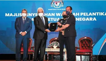  ?? ?? New role: hamzah (second from left) presenting the appointmen­t letter to comm razarudin while acryl sani (second from right) and home ministry secretary-general datuk seri Wan ahmad dahlan abdul aziz look on during the ceremony in Putrajaya.