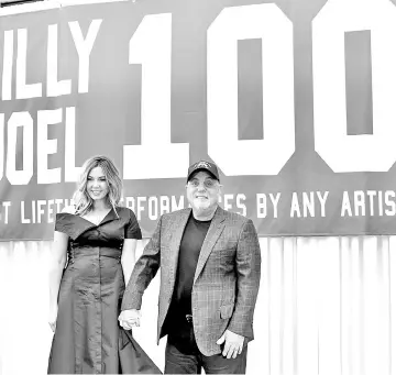  ??  ?? Billy Joel and wife Alexis Roderick pose in front of the banner during a press conference honouring Joel’s 100th Lifetime Performanc­e at Madison Square Garden on Wednesday in New York City. • Billy Joel (left) and New York Governor Andrew Cuomo pose...