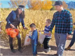  ??  ?? Ashley Wagner, left, gives out candy to Aaron Candelaria Jr. and Aiden Murillo, with Arron Candelaria, in the corn maze at Wagner’s Farmland Experience in Corrales during the Halloween Extravagan­za on Sunday.