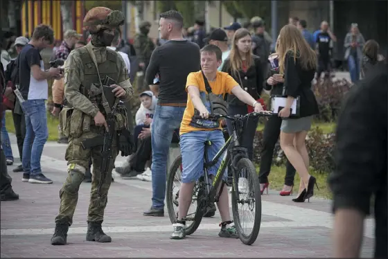  ?? THE ASSOCIATED PRESS ?? A Russian soldier stands guard in May as civilians walk in the center of Melitopol, Ukraine, in territory under Russian military control. As Russians seized parts of eastern and southern Ukraine, mayors, civilian administra­tors and others, including nuclear power plant workers, say they have been abducted, threatened or beaten to force their cooperatio­n.