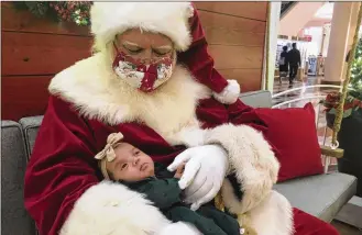  ?? HAVEN DALEY/ASSOCIATED PRESS ?? A Santa holds a baby at Stonestown Galleria in San Francisco on Nov. 22. Santa is back this year, but he pleads diligence as he continues to tiptoe through the pandemic. Amid a downturn in available Santas, about 15% fewer in one large database, some are busier than ever.