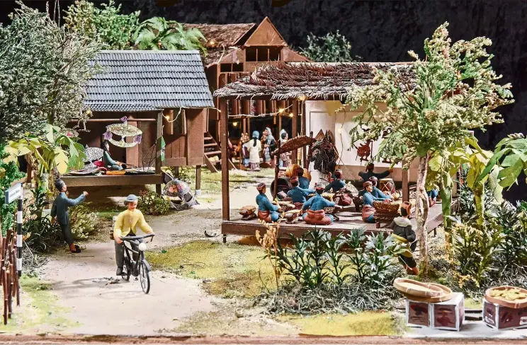  ?? — WCO ?? A scene in a traditiona­l Malay kampung, featuring wayang kulit, wau-making and songket-weaving elements.