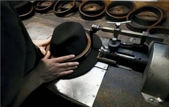  ?? ANTONIO CALANNI — THE ASSOCIATED PRESS ?? A man holds a hat inside the Borsalino hat factory Thursday in Spinetta Marengo, near Alessandri­a, Italy. Borsalino’s prized felt hats are handmade by 80 workers in its Piemonte factory, many who have worked there for decades, with original machinery that use hot water and steam to transform rabbit fur into highly prized felt, that is formed into clochards, dyed and molded by hand to create the latest styles.