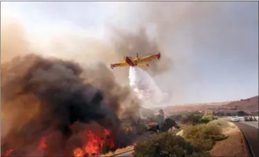  ?? RINGO H.W. CHIU — THE ASSOCIATED PRESS ?? An air tanker drops water on a fire along the Ronald Reagan (118) Freeway in Simi Valley Monday.