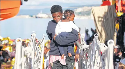  ??  ?? A woman carries a child up a gangplank as migrants land in Vibo Marina, Italy, after a rescue operation in the Mediterran­ean Sea on Saturday.