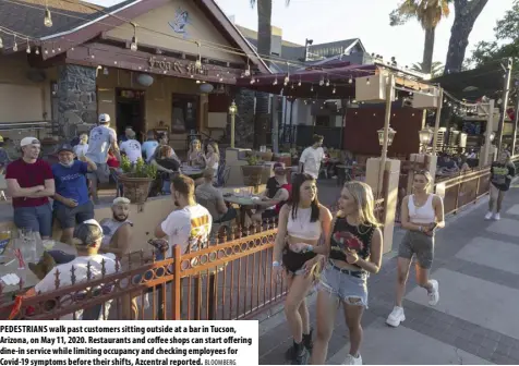  ?? BLOOMBERG ?? PEDESTRIAN­S walk past customers sitting outside at a bar in Tucson, Arizona, on May 11, 2020. Restaurant­s and coffee shops can start offering dine-in service while limiting occupancy and checking employees for Covid-19 symptoms before their shifts, Azcentral reported.