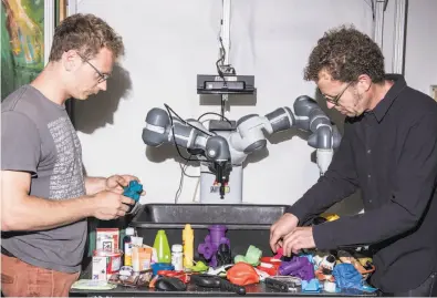  ?? Jason Lecras / New York Times ?? Jeff Mahler (left) and Ken Goldberg arrange objects for a robot to grasp at UC Berkeley. The techniques they’re using to train the robot represent a fundamenta­l shift in robotics research.