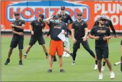  ?? The Associated Press ?? PRESSING CONCERNS FOR PROS: Baltimore Orioles manager Brandon Hyde, center in orange shorts, looks on as his team warms up during training camp Tuesday in Baltimore.