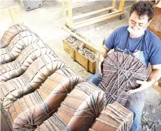  ??  ?? A worker applies stretched strings to freshly glued guitar bodies to keep the parts in place.